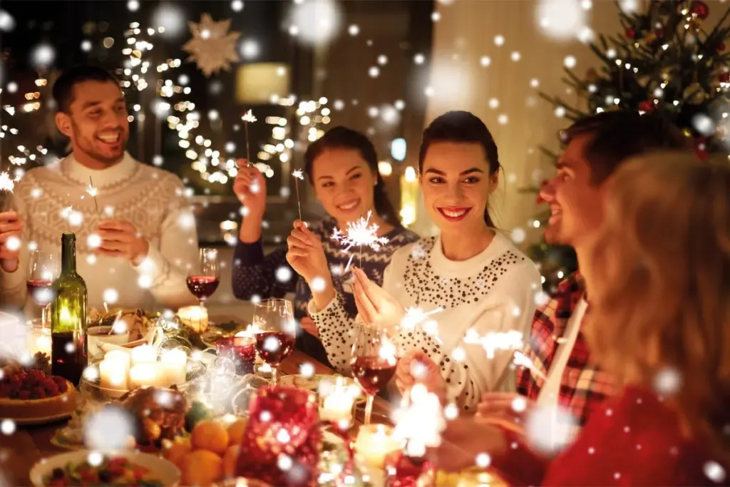 Weihnachtliche Weihnachtsfeier mit mehreren lächelnden Personen, die mit Getränken zusammenkommen und festlich dekorierte Umgebung mit Lichtern im Hintergrund.