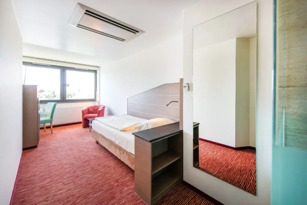 Modernes Einzelzimmer in einem Hotel am Rhein mit hellen Wänden, großem Fenster und minimalistischer Einrichtung.